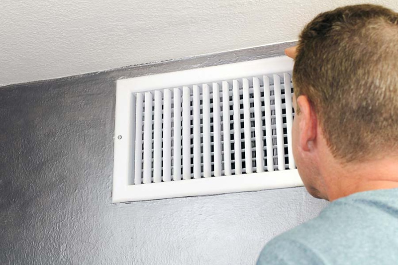 man in bliue shirt looking at white wall vent